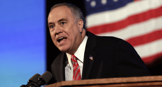 man speaking in front of american flag